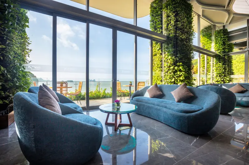 Sảnh chờ với ghế sofa xanh, tường cây xanh và vách kính lớn nhìn ra biển ở Flamingo Cát Bà