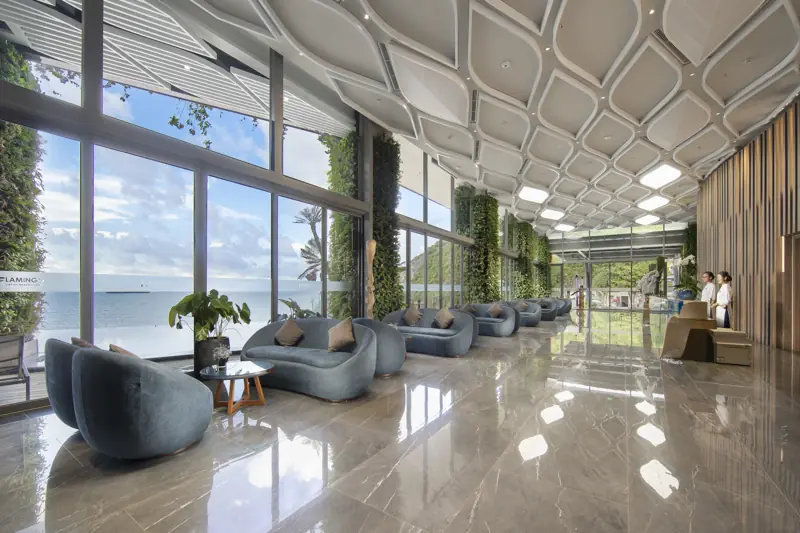 Sảnh Flamingo Cát Bà sàn đá bóng, sofa xanh và vách kính lớn nhìn ra biển