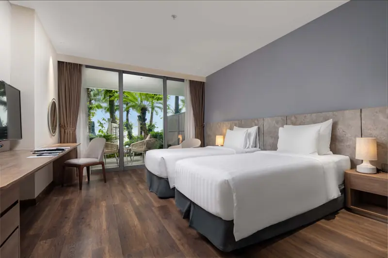 Phòng Premier Beach Front: hai giường đơn, cửa kính mở ra vườn dừa sát bãi biển