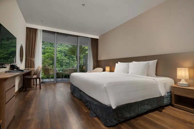 Phòng Premier Mountain View: giường đôi lớn, cửa kính nhìn ra vách núi phủ cây