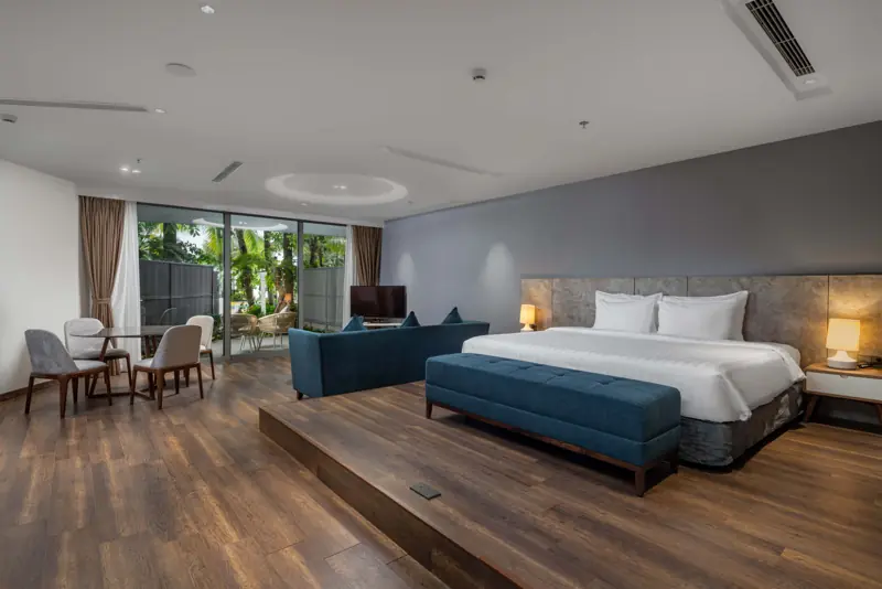 Căn Premier Residence Beach Front: giường đôi trên bục gỗ, sofa xanh, cửa kính mở ra vườn sát biển