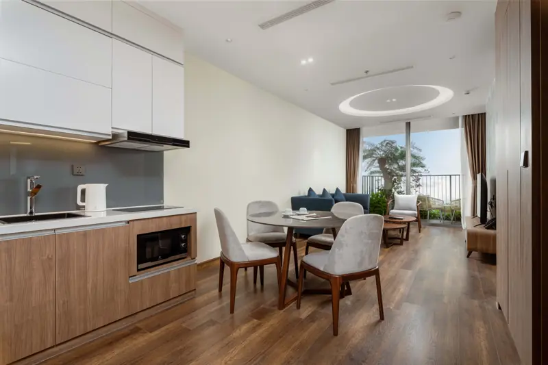 Căn Premier Residence 1 phòng ngủ: góc bếp, bàn ăn bốn ghế và phòng khách mở ra ban công
