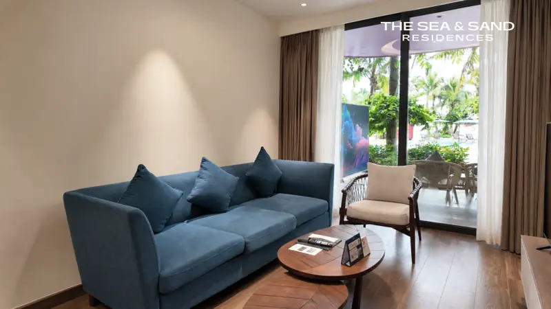 Phòng khách căn The Sea & Sand: sofa xanh, cửa kính mở ra vườn
