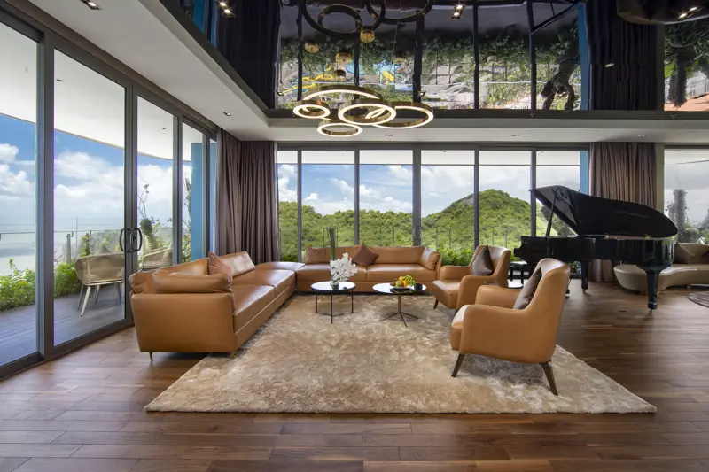 Phòng khách Imperial Suite với sofa da, đàn piano và cửa kính nhìn ra núi đá và biển